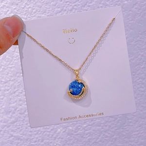 Dettaglio di una collana con ciondolo pianeta blu celeste e cristalli di zircone su oro