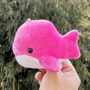 Handheld view of a pink plush whale keychain with soft fuzzy texture outdoors