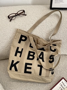 Khaki canvas tote bag with black letter print on a minimalist sofa background
