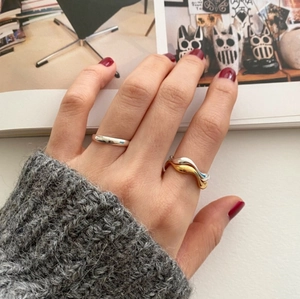 Detail of silver wavy ring and minimalist band on hand with grey sweater