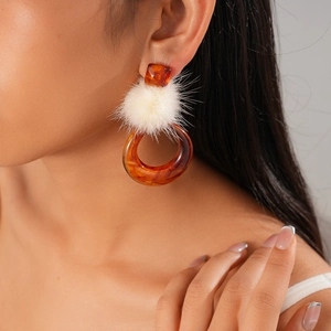 Close-up of amber resin hoop earrings with white fur ball accent on a model