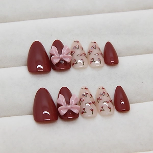 Press-on nail set with red polish, resin bows, and cherry designs on a white stand