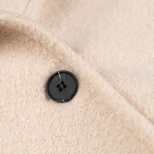 Dettaglio ravvicinato del tessuto in pile beige e bottone in resina nera del cappotto