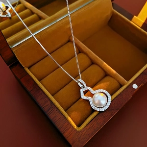 Detailed macro view of a silver gourd necklace with pearl and diamonds in a wooden box