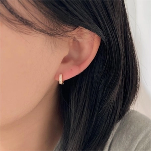 Detailed close-up of a gold-plated huggie earring with zircons on a model ear