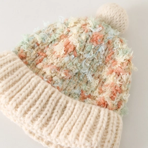 Detailopname van dikke veelkleurige gebreide muts met textuur en grote zachte pompon
