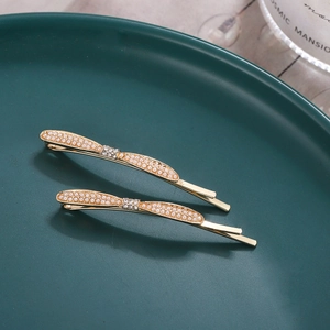 Vintage style gold metal hair clips with delicate pearls and rhinestones on a ceramic dish