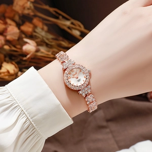 Elegant rose gold rhinestone women's watch with white dial on wrist with dried flowers