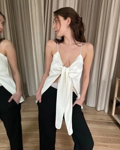 Close-up of a white satin crop top featuring a large bow design and thin straps