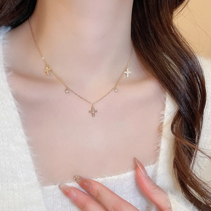 Close-up of gold cross necklace with small round zircon pendants on a white sweater