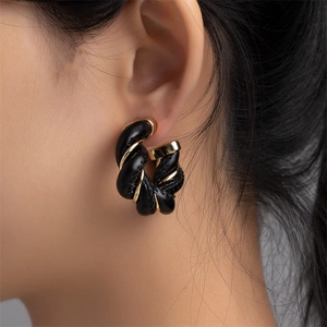 Close-up of twisted gold metal and black leather woven hoop earrings on a model