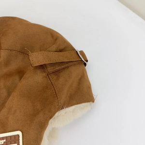 Detailed close-up of brown suede trapper hat with soft faux fur lining and metal buckle