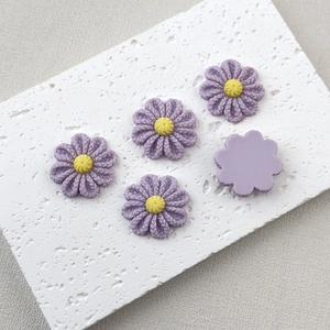 Macro shot of purple resin daisy flower charms with yellow center on white stone plate