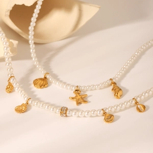 Double-layer pearl necklace with gold starfish and shell charms on beige textured background