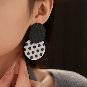 Close-up of black and white polka dot acrylic earrings worn by a model in soft light