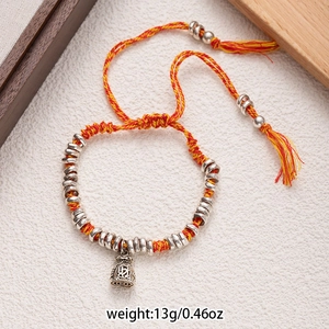 Detail of woven lucky red cord bracelet with silver fortune bag charm and lucky ring