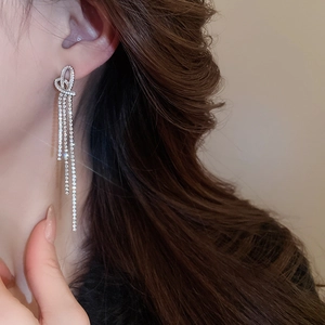 Close-up of heart-shaped silver earrings with long sparkling rhinestone tassels on model