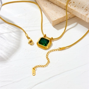 Retro gold snake chain necklace with square emerald zircon pendant on stone background