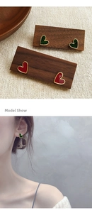 Close-up of heart earrings in red and dark green on walnut wood and a model's ear