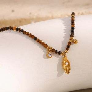 Close-up of tiger eye stone beads and a 18K gold-plated Hamsa hand pendant with zircon