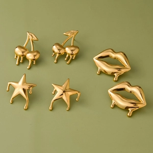 Detail of gold dripping earrings set featuring cherry, star, and lip shapes in high polish