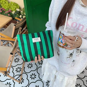 Green striped canvas makeup bag held in a cafe setting, outdoor lifestyle detail view