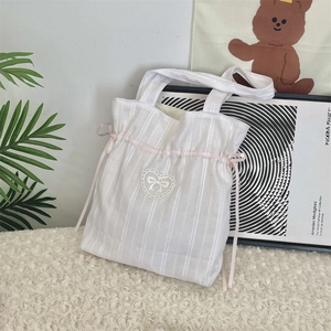 Dettaglio della borsa in tela a righe bianche con nastro di seta rosa e cuore di pizzo