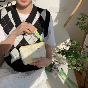 Detail of floral makeup bag with yellow zipper, green strap and cream fabric texture