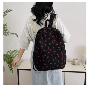 Detail of strawberry print on black corduroy backpack worn by a female model