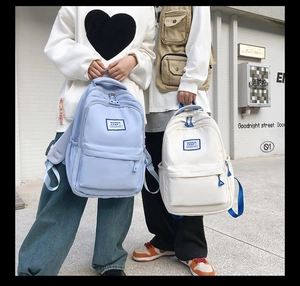 Detail of light blue and beige nylon backpacks featuring branded woven label and large pockets