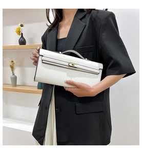 Detail of white structured handbag with top handle and metal clasp held by model in black suit