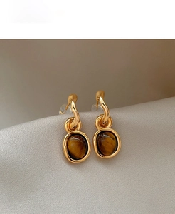 Macro shot of gold plated oval tiger eye earrings on soft silk fabric texture