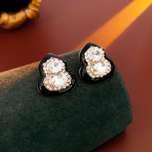 Close-up of gourd earrings with black enamel and crystals on green velvet stand