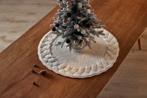 Close-up of white knitted Christmas tree skirt with cable knit pattern on dark wood