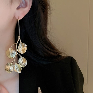Close-up of a model wearing a golden metal leaf earring featuring a minimalist design