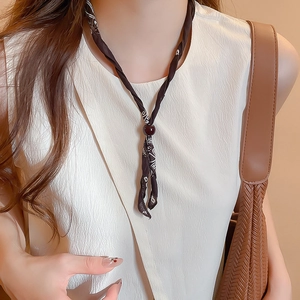 Detail of coffee brown paisley silk scarf necklace with a central bead on a model neck