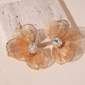Detailed close-up of large golden floral earrings with clear crystal centers on stone