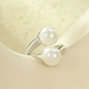 Detailed view of silver open ring with dual pearls on a minimalist ceramic edge
