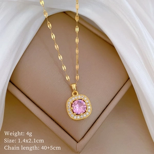 Detail of gold pendant with a pink gemstone in a beige jewelry box with product specs