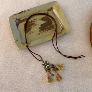 Detail der Boho-Halskette mit Bronze-Blumenanhänger und Baumwoll-Quasten-Verlauf