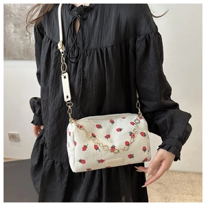 Detail of strawberry print corduroy crossbody bag featuring a gold chain and logo