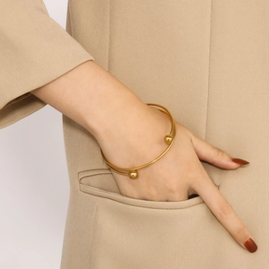 Detail of a minimalist gold double-layer steel ball bracelet styled with a beige suit