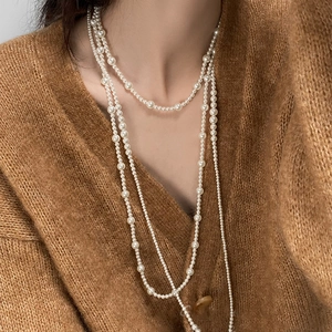 Detail of layered white pearl necklace worn over a brown knit sweater for a minimalist look
