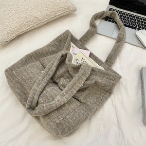 Top view of a large grey plush tote bag with two front pockets on a white bed surface