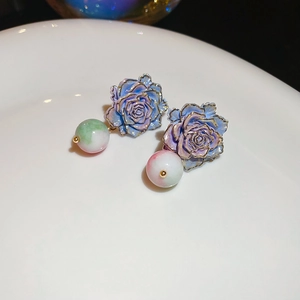Detail of rose-shaped earrings with gold edges and marbled beads on white ceramic