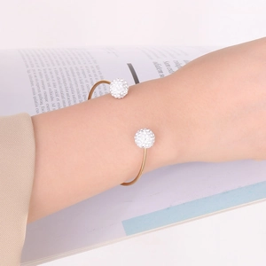 Detail of a gold open cuff bracelet with sparkling disco ball charms on a model wrist