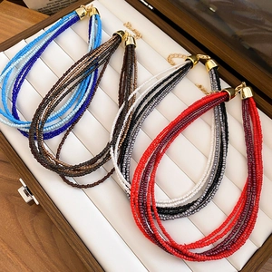 Detail of multi-layered seed bead necklaces in blue, brown, grey and red with gold clasps