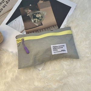 Close-up of lightweight grey plaid packing cube with neon zipper and woven label