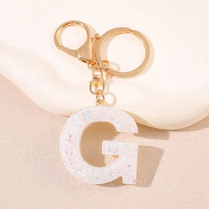 Vue macro d'un porte-clés lettre G en résine pailletée blanche avec fermoir doré chic