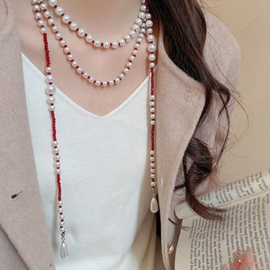 Detail of multi-layer necklace with white pearls, red faceted beads and teardrop pendant